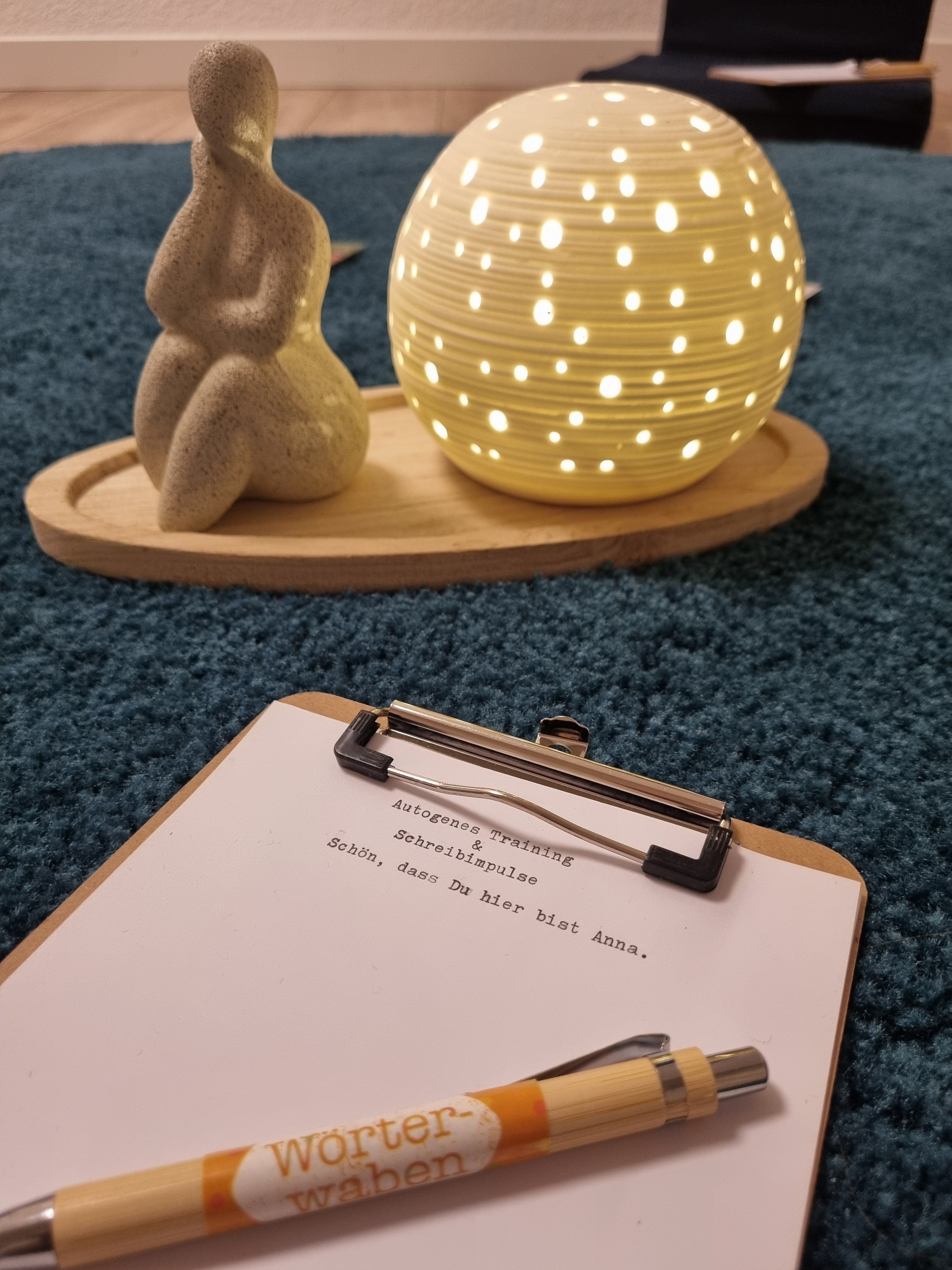 Meditative Atmosphäre mit Leuchtkugel, Figur und Klemmbrett mit Willkommensnachricht und Wörterwaben-Stift.