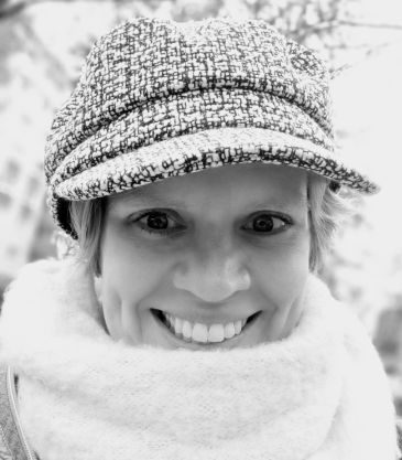 Eine Person mit Mütze und Schal lächelt direkt in die Kamera. Das Bild ist in Schwarzweiß gehalten.